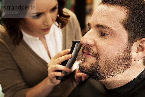 Nahaufnahme eines weiblichen Friseurs beim Bartschneiden des Bartes einer männlichen Kundin im Salon