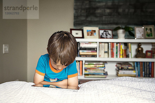 Junge benutzt Tablet-Computer  während er zu Hause auf dem Bett liegt
