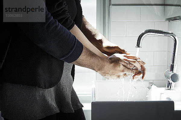 Mittelteil eines Liebespaares beim Händewaschen im Badezimmer