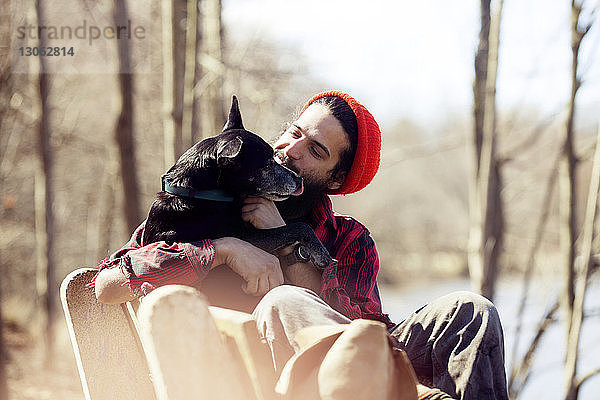 Anhänglicher Mann schaut Hund an  während er während des Urlaubs im Wald auf einer Bank sitzt