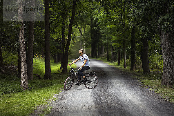 Glücklicher Mann fährt Fahrrad auf Straße im Wald