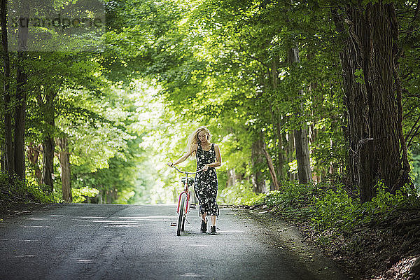 Frau mit Fahrrad auf Straße inmitten von Bäumen