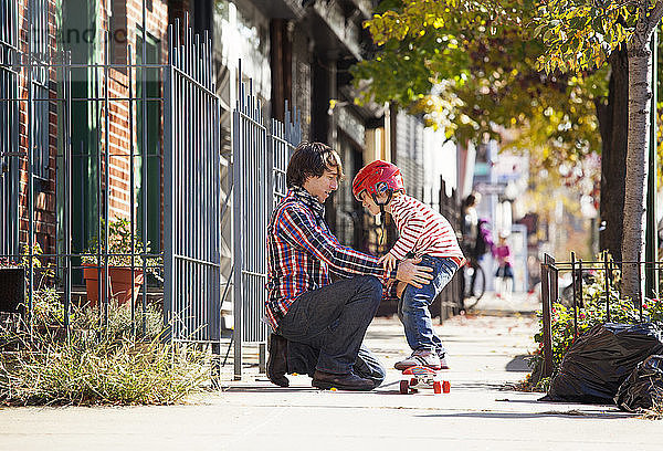 Vater hilft Sohn beim Stehen auf dem Skateboard