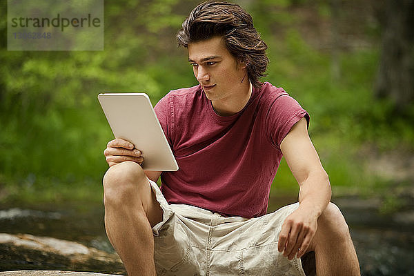 Junger Mann benutzt Tablet-Computer  während er auf Steinen sitzt