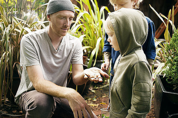 Mann zeigt Kindern Regenwurm im Garten