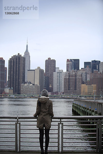 Rückansicht einer am Geländer stehenden Frau gegen das Stadtbild