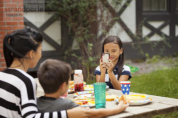 Lächelndes Mädchen fotografiert Familie  während es am Picknicktisch sitzt