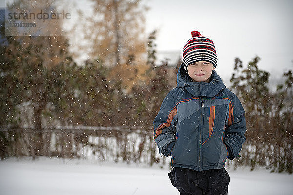 Porträt eines lächelnden Jungen in warmer Kleidung auf schneebedecktem Feld stehend