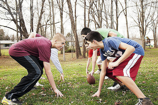 Lächelnde Freunde spielen American Football  während sie sich im Park über das Spielfeld beugen