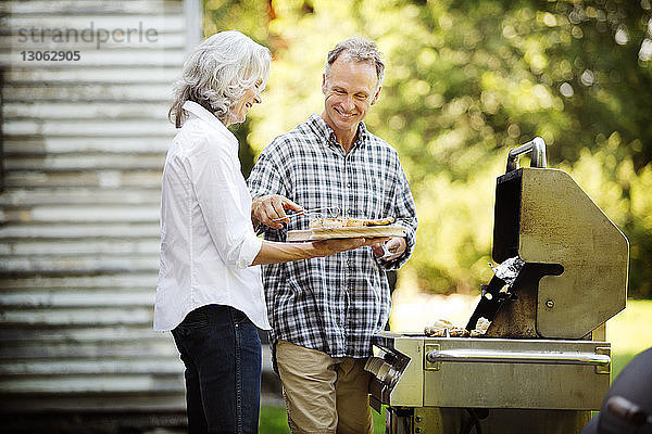 Glückliches älteres Ehepaar beim Zubereiten von Speisen  während es im Garten am Barbecue-Grill steht