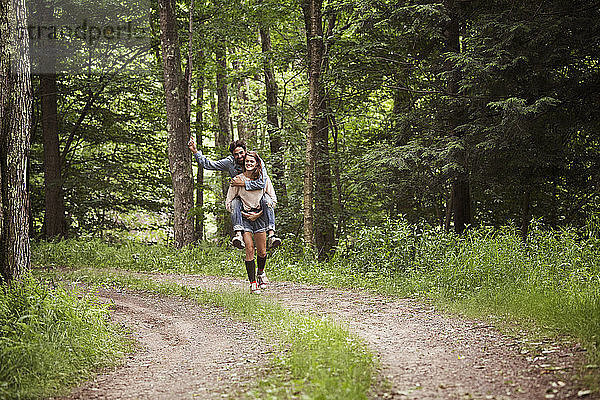 Frau nimmt Mann huckepack  während sie auf Feldweg im Wald geht