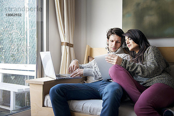 Frau zeigt ihrem Freund zu Hause auf dem Sofa ein digitales Tablet