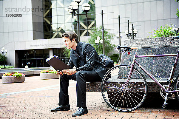 Geschäftsmann hält Ordner  während er mit dem Fahrrad auf dem Sitz sitzt