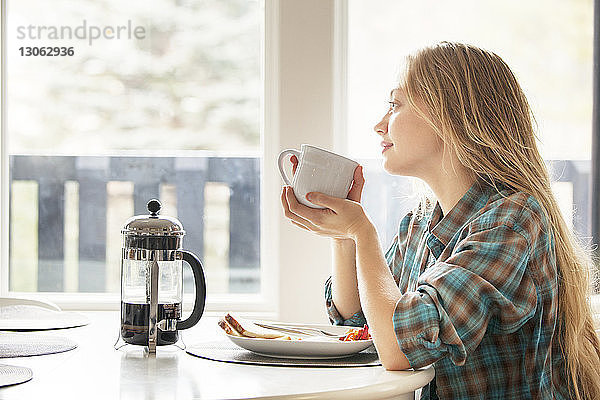 Nachdenkliche Frau schaut weg  während sie zu Hause eine Kaffeetasse hält