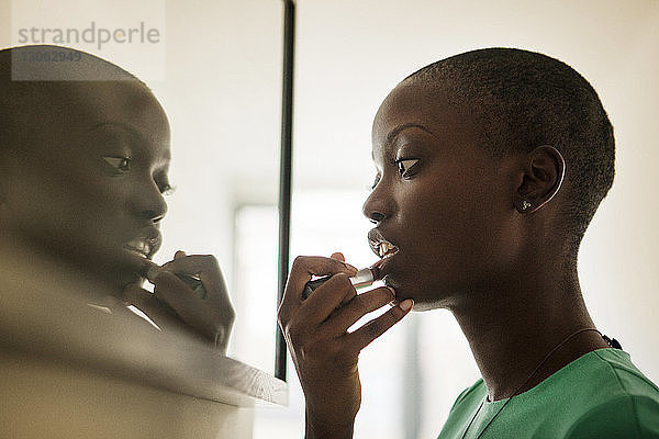 Seitenansicht einer Frau  die Lippenstift aufträgt  während sie zu Hause am Spiegel steht