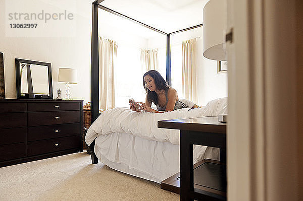 Glückliche Frau benutzt Telefon am Bett im Schlafzimmer