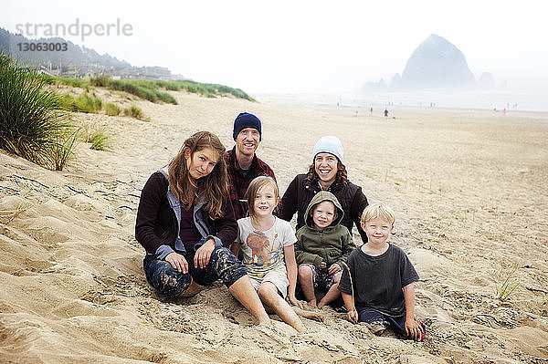 Porträt einer Familie  die auf Sand am Strand sitzt