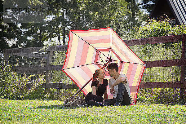 Paar mit Schirm sitzt auf dem Feld gegen den Zaun