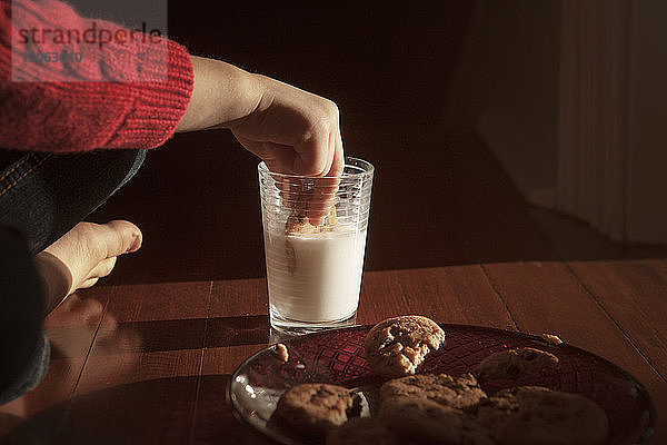 Ausgeschnittenes Bild eines Mädchens  das Kekse in Milch taucht  während es auf dem Boden sitzt