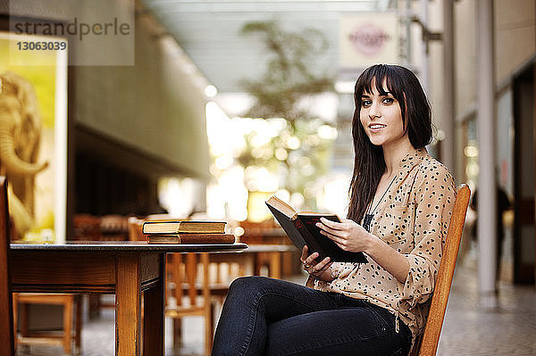 Porträt einer Frau  die ein Buch hält  während sie auf einem Stuhl im Strassencafé sitzt