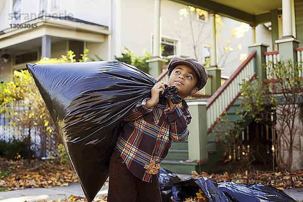 Junge schaut weg  während er einen Müllsack im Hof trägt