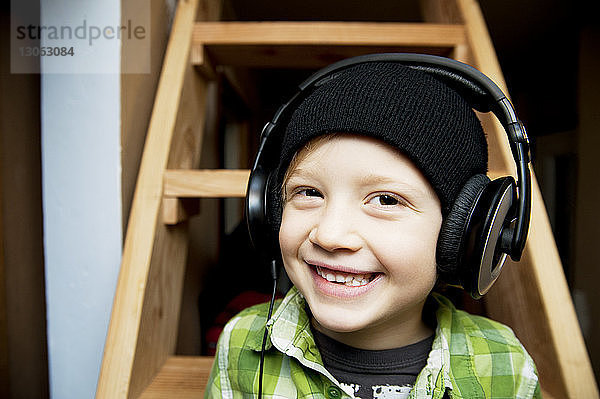 Porträt eines glücklichen Jungen  der zu Hause gegen eine Leiter Musik hört