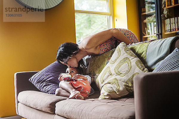 Mutter küsst Sohn  der zu Hause auf dem Sofa liegt