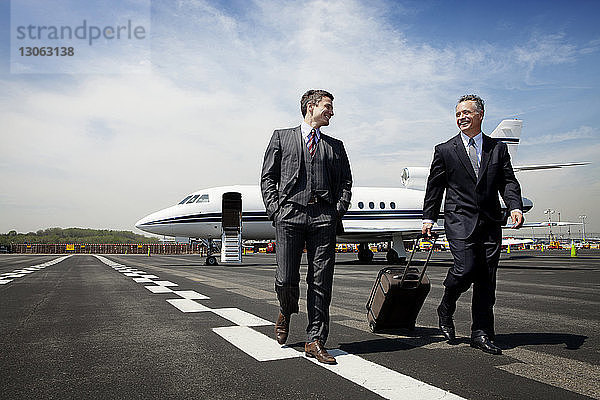 Glückliche Geschäftsleute laufen auf der Startbahn eines Flughafens gegen den Himmel