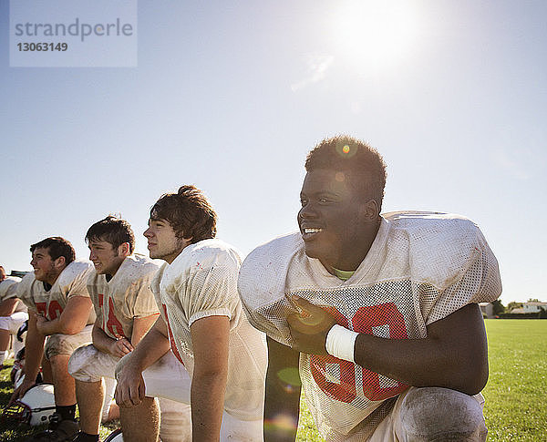 Lächelnde Sportler  die bei Sonnenschein auf dem Spielfeld vor dem Himmel knien