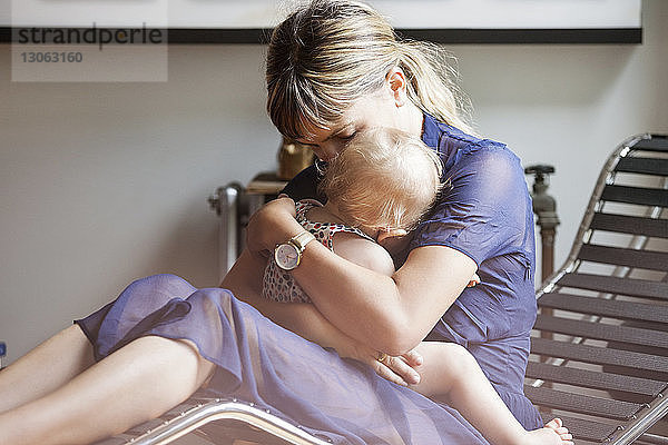 Mutter umarmt Tochter  während sie zu Hause auf einem Liegestuhl sitzt