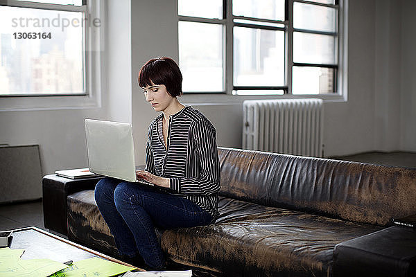 Geschäftsfrau benutzt Laptop  während sie im Kreativbüro auf dem Sofa sitzt