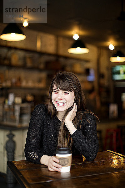 Lächelnde Frau mit Kaffee in der Hand und am Tisch im Café sitzend