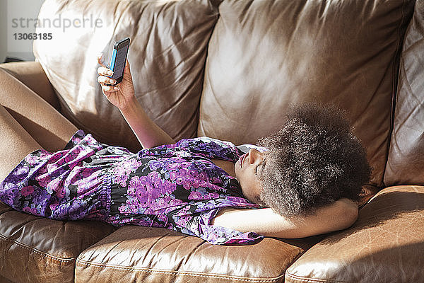 Frau benutzt Mobiltelefon  während sie sich zu Hause auf dem Sofa entspannt