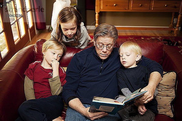 Hochwinkelansicht eines Großvaters  der Kindern Geschichten erzählt  während er zu Hause auf dem Sofa sitzt
