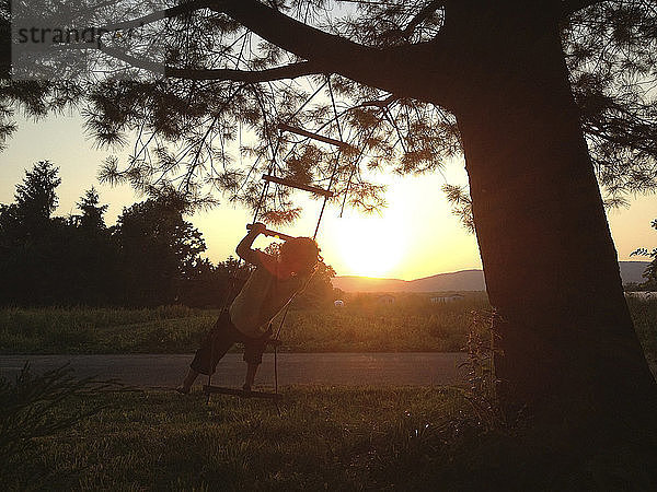 Rückansicht eines Jungen  der bei Sonnenuntergang auf eine Strickleiter auf dem Feld klettert