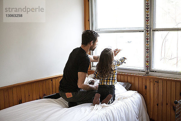 Rückansicht von Vater und Sohn  die auf Fensterglas zeichnen  während sie auf dem Bett knien