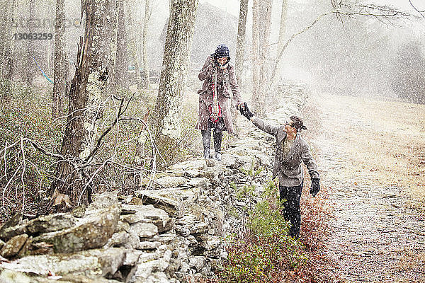 Mann hilft Frau  die im Winter auf einer Steinmauer läuft