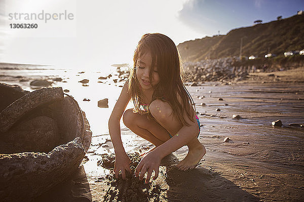 Mädchen spielt bei Sonnenuntergang im Sand am Strand