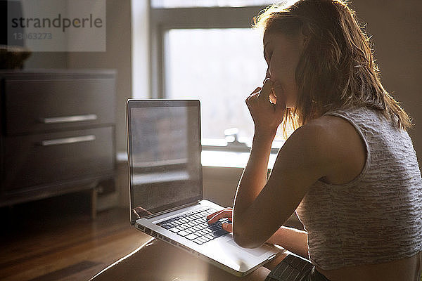 Nachdenkliche Frau benutzt Laptop  während sie zu Hause sitzt