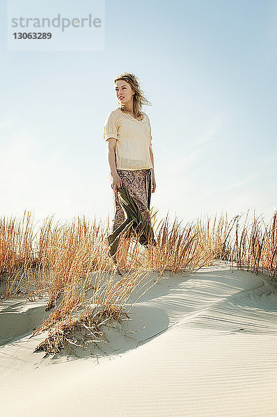 Frau schaut weg  während sie mit einem Schal auf Sand gegen den Himmel steht