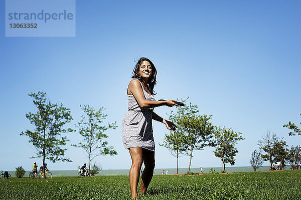 Verspielte Frau wirft Plastikscheibe  während sie im Park steht