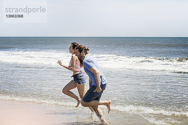 Seitenansicht eines Paares  das während der Sommerferien am Strand an Land läuft