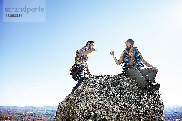 Freunde machen einen Faustschlag  während sie auf einem Felsen gegen den klaren Himmel sitzen