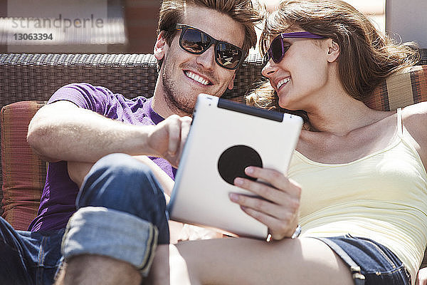 Glückliches Paar benutzt Tablette  während es auf dem Sofa im Hinterhof sitzt