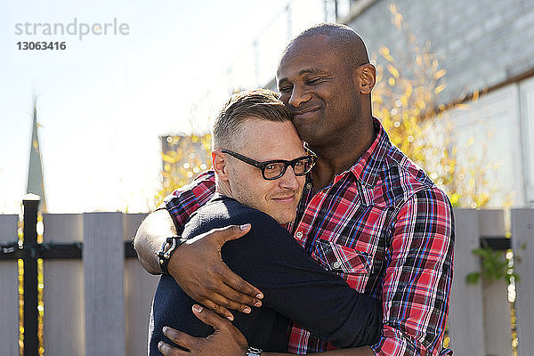 Lächelnde schwule Männer umarmen sich am Zaun