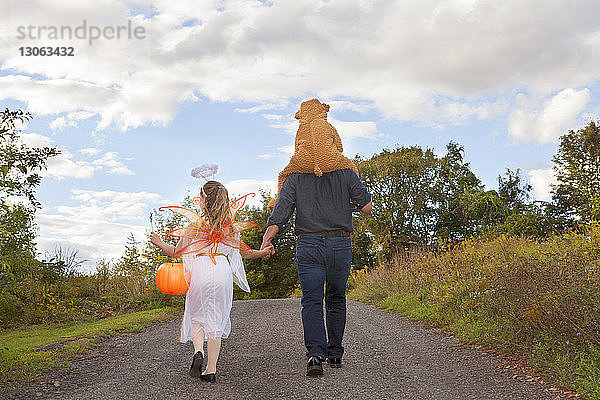 Rückansicht eines Vaters mit Kindern im Halloween-Kostüm beim Spaziergang auf dem Feld