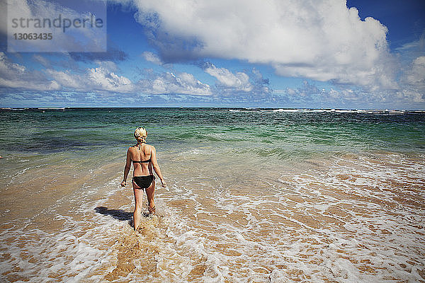 Rückansicht einer Frau im Bikini  die gegen den bewölkten Himmel in Richtung Meer läuft