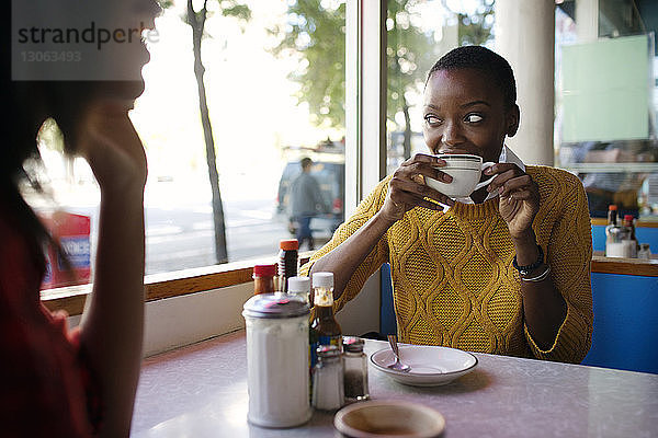 Frau schaut beim Cappuccino-Trinken weg  während sie mit einem Freund im Café sitzt