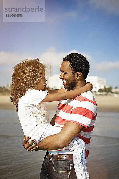 Mann trägt Tochter  während er am Strand gegen den Himmel steht