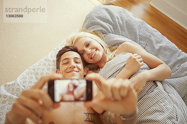 Hochwinkelansicht eines Paares  das im Bett liegt und fotografiert